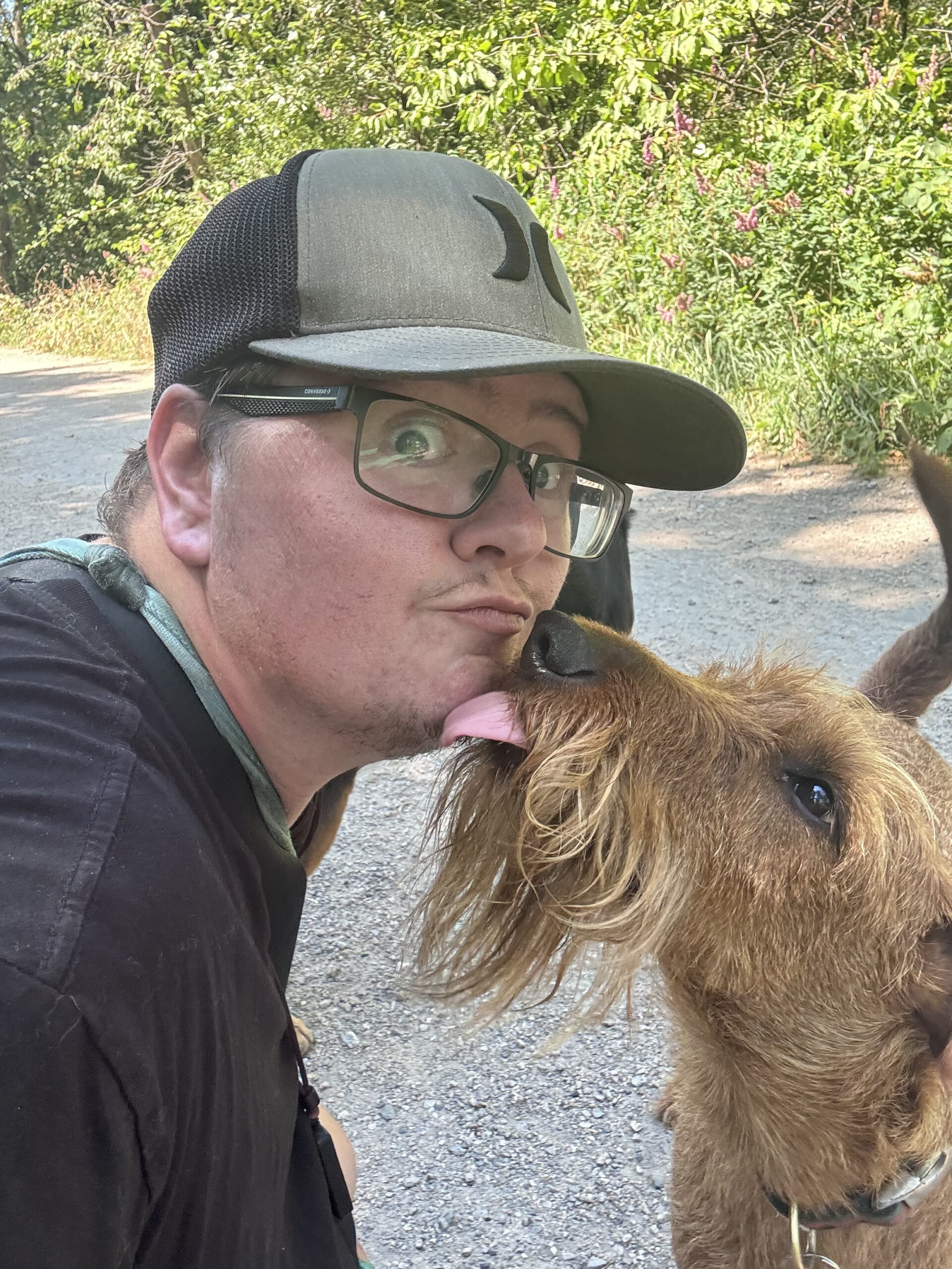 Douglas Fur Pets co-owner Nick making a silly face while being licked by an Irish Terrier during a dog walk in Vancouver, showing the fun and loving bond between walker and dog.